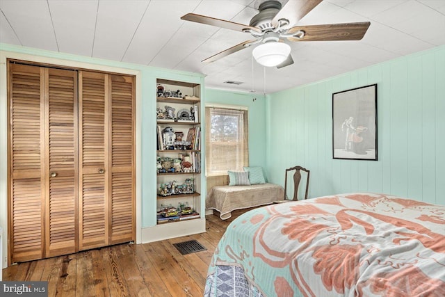 bedroom with hardwood / wood-style flooring, ceiling fan, wooden walls, and a closet