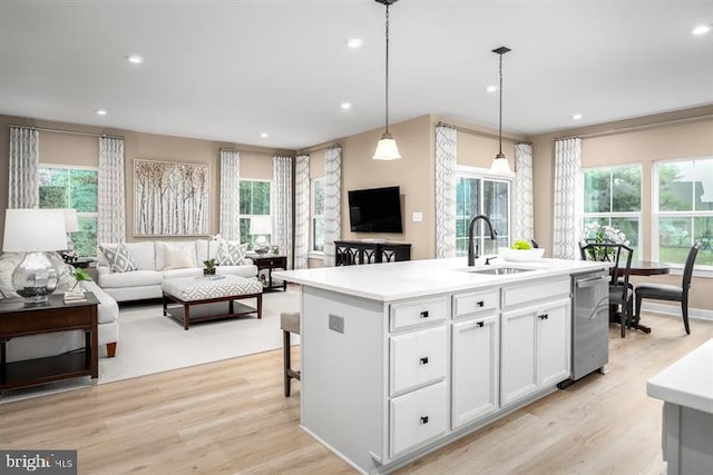 kitchen featuring pendant lighting, sink, a kitchen island with sink, white cabinetry, and light wood-type flooring