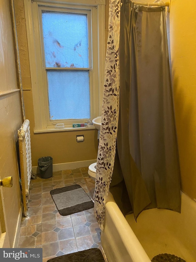 bathroom featuring shower / bath combination with curtain, a healthy amount of sunlight, toilet, and radiator