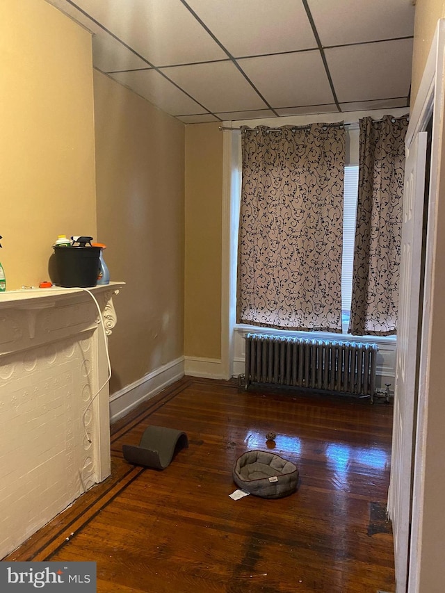 interior space with hardwood / wood-style floors, a drop ceiling, and radiator heating unit