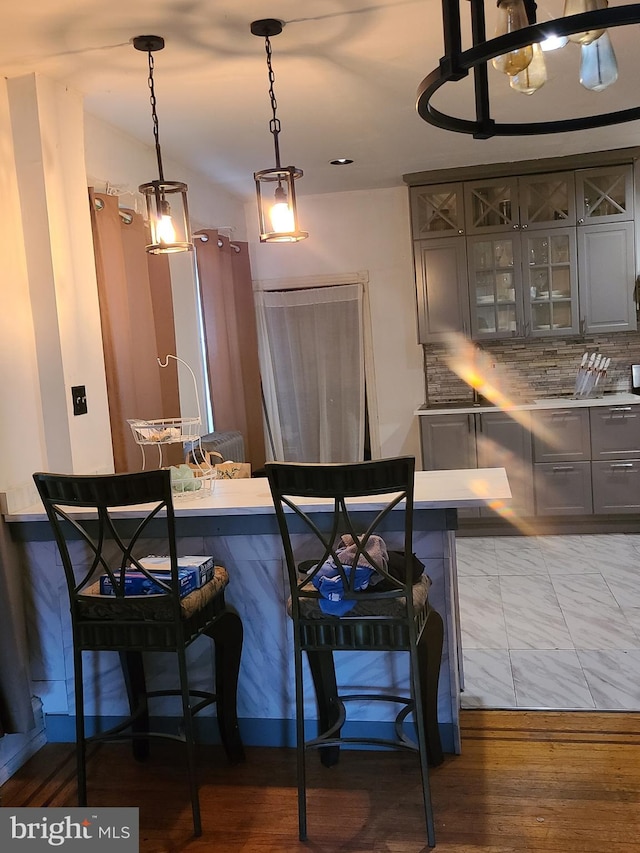 kitchen with hardwood / wood-style flooring, decorative light fixtures, backsplash, and a breakfast bar