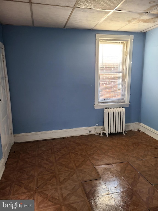 spare room featuring a paneled ceiling, radiator heating unit, and parquet floors