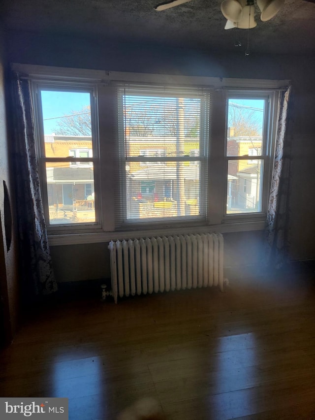 unfurnished room featuring radiator heating unit, ceiling fan, a wealth of natural light, and hardwood / wood-style floors