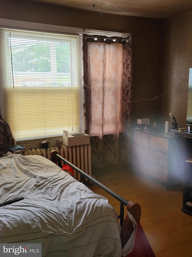 bedroom featuring radiator heating unit and hardwood / wood-style flooring