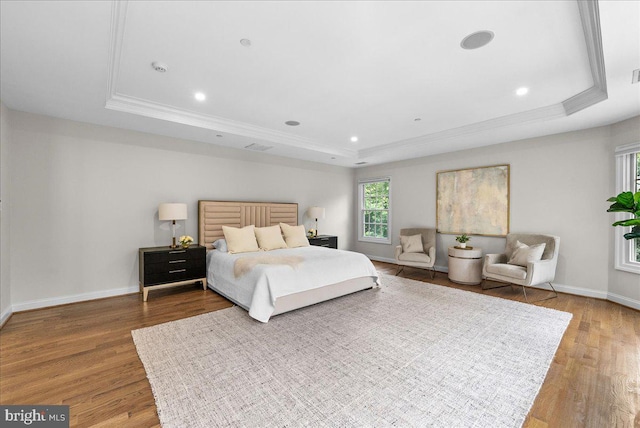 bedroom featuring ornamental molding, wood-type flooring, and a raised ceiling