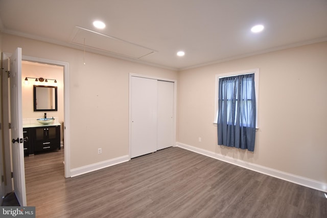 unfurnished bedroom with ensuite bathroom, sink, crown molding, dark hardwood / wood-style flooring, and a closet