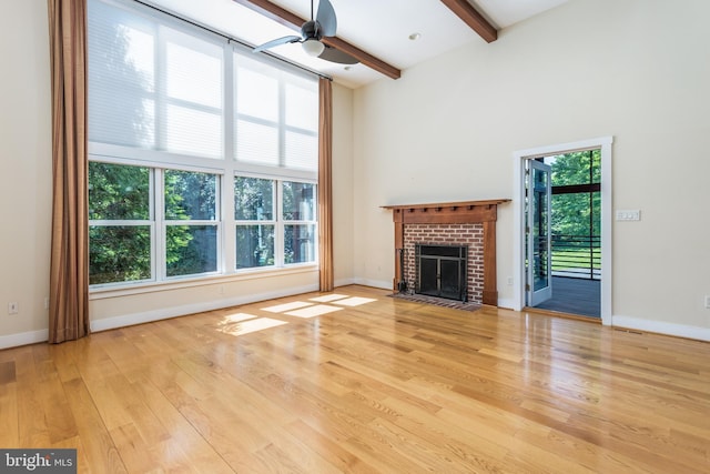 unfurnished living room with a fireplace, a high ceiling, light wood-type flooring, and plenty of natural light