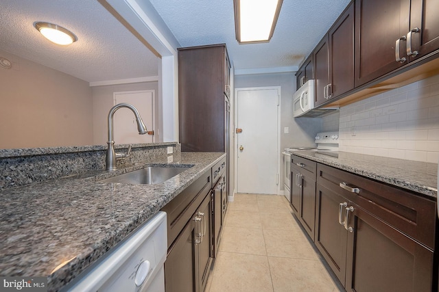 kitchen with sink, dark stone counters, a textured ceiling, white appliances, and light tile patterned floors