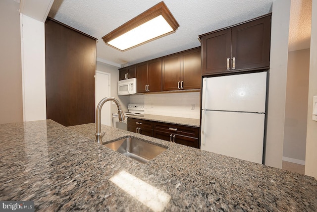 kitchen with tasteful backsplash, dark stone counters, dark brown cabinets, white appliances, and sink