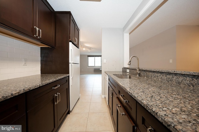 kitchen with dark stone countertops, sink, light tile patterned floors, and white refrigerator