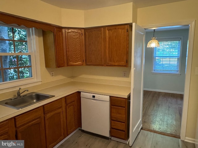 kitchen with white dishwasher, decorative light fixtures, light wood-type flooring, and sink