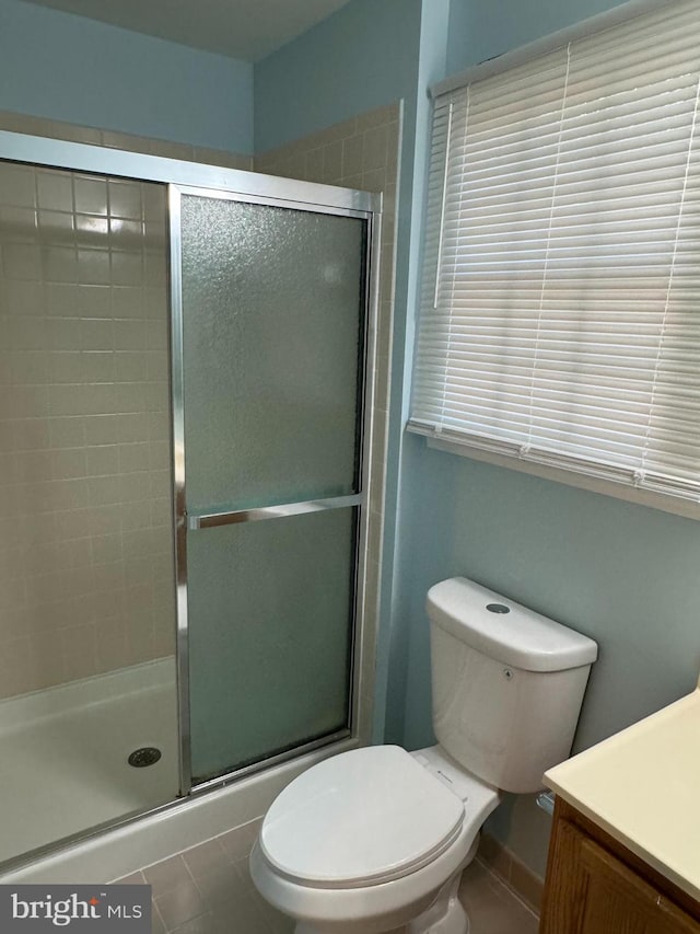 bathroom with tile patterned floors, vanity, toilet, and a shower with door