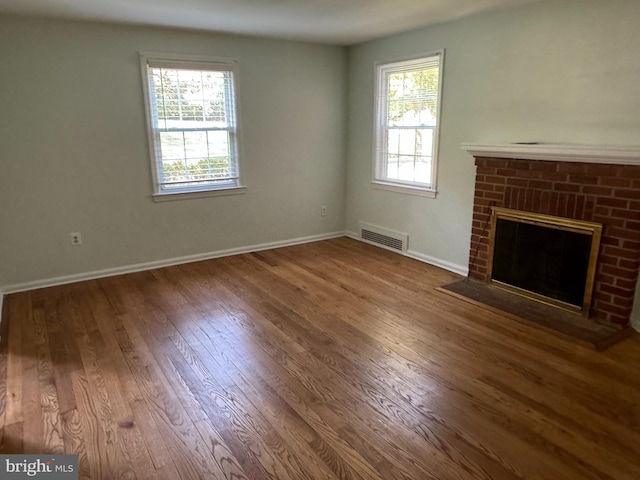 unfurnished living room featuring wood-type flooring and a brick fireplace