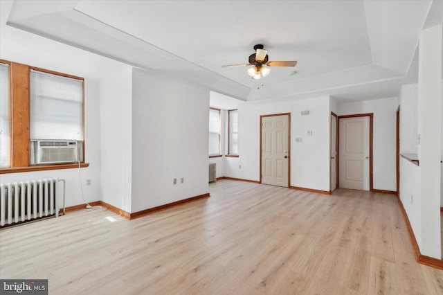 unfurnished room featuring a tray ceiling, radiator, light hardwood / wood-style flooring, and cooling unit