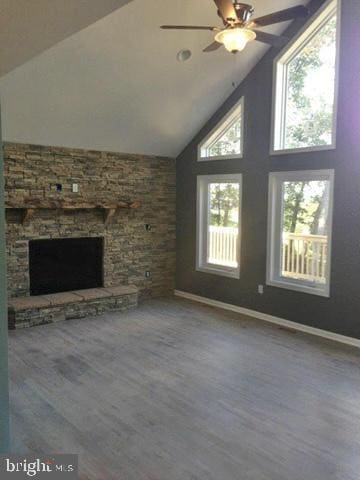 unfurnished living room featuring a healthy amount of sunlight, a stone fireplace, wood-type flooring, and high vaulted ceiling