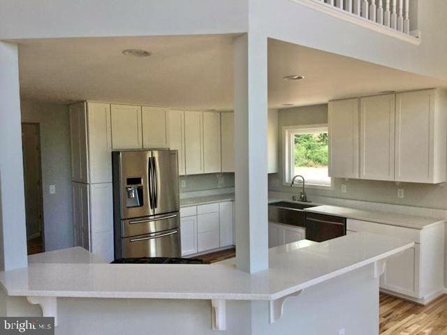 kitchen featuring dishwasher, stainless steel refrigerator with ice dispenser, a breakfast bar area, white cabinets, and light wood-type flooring