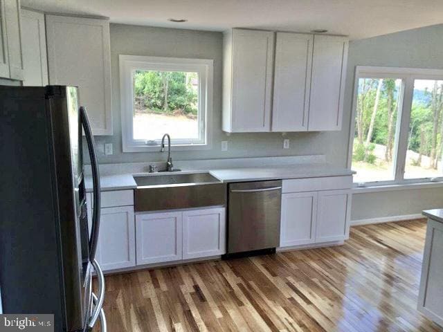 kitchen featuring black refrigerator, stainless steel dishwasher, sink, light hardwood / wood-style floors, and white cabinetry