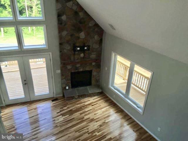 unfurnished living room featuring french doors, a healthy amount of sunlight, lofted ceiling, and light hardwood / wood-style flooring