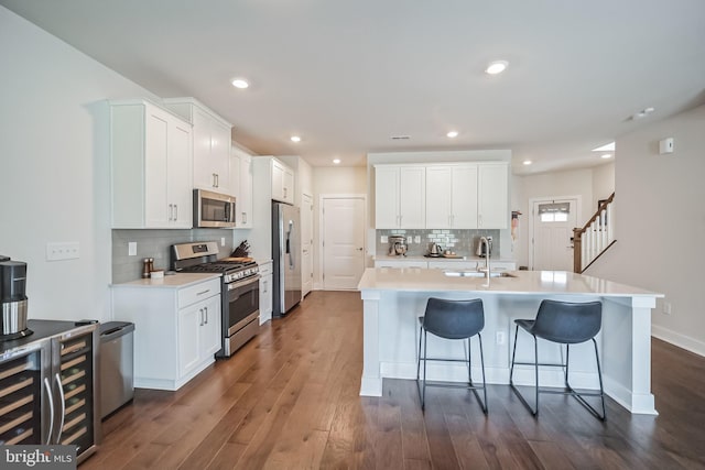 kitchen featuring appliances with stainless steel finishes, dark hardwood / wood-style floors, white cabinetry, and a kitchen island with sink