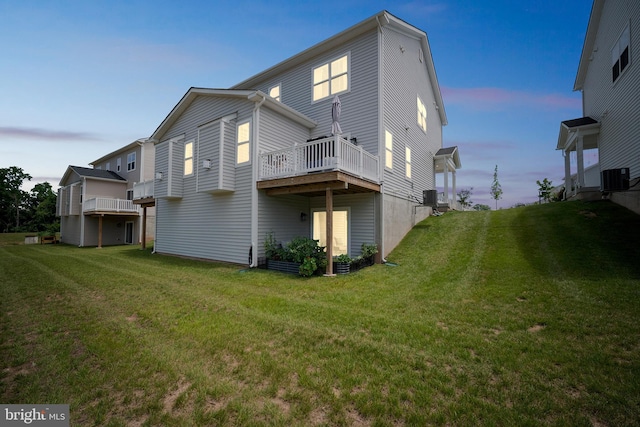 back house at dusk with a yard, central AC unit, and a deck