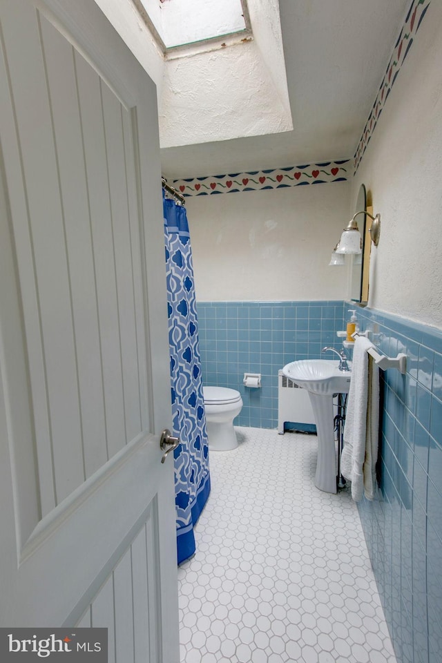 bathroom with tile patterned flooring, toilet, and tile walls