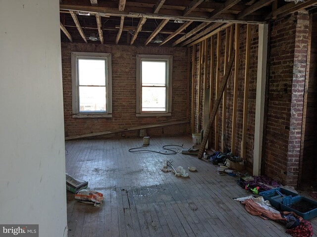 miscellaneous room with wood-type flooring and brick wall