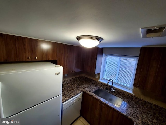 kitchen with dishwasher, dark stone counters, sink, dark brown cabinets, and stainless steel refrigerator