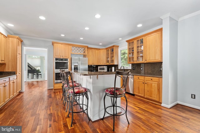 kitchen featuring ornamental molding, dark wood-type flooring, appliances with stainless steel finishes, and a breakfast bar area