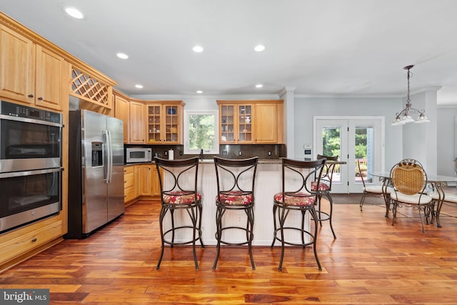 kitchen with decorative backsplash, pendant lighting, stainless steel appliances, and light hardwood / wood-style flooring