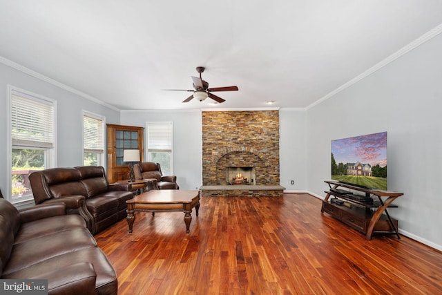 living room with ceiling fan, a stone fireplace, wood-type flooring, and crown molding