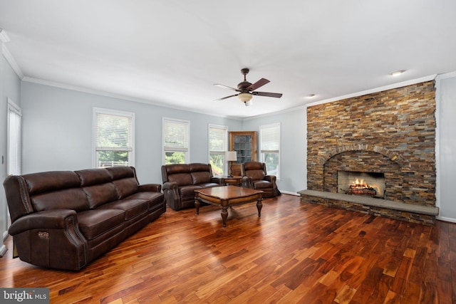 living room with ceiling fan, a stone fireplace, wood-type flooring, and ornamental molding