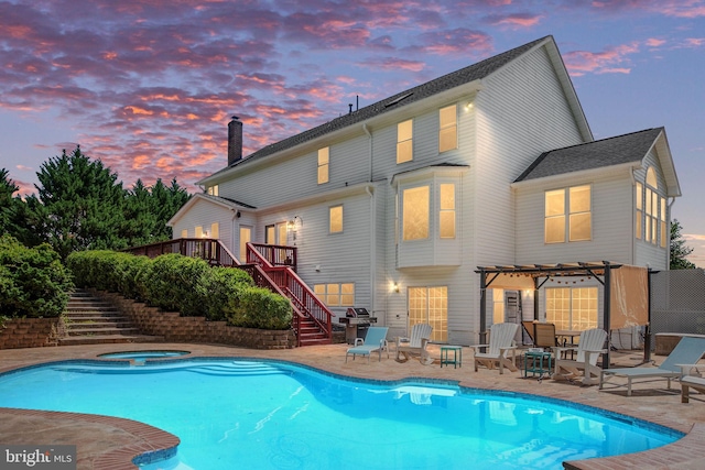 pool at dusk featuring an in ground hot tub, a pergola, a patio, and a wooden deck