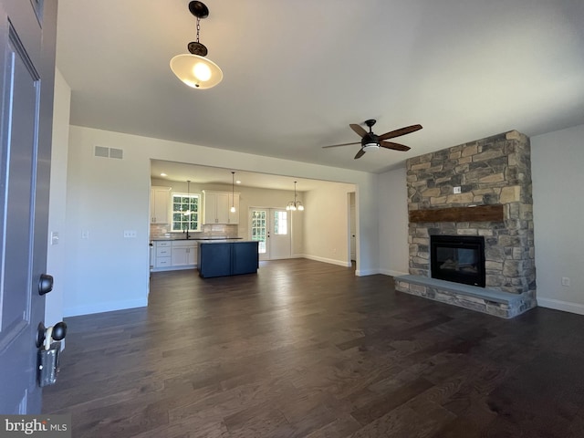 unfurnished living room with a stone fireplace, dark hardwood / wood-style floors, and ceiling fan