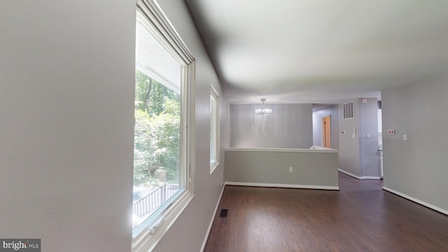 spare room with an inviting chandelier, plenty of natural light, and dark hardwood / wood-style floors