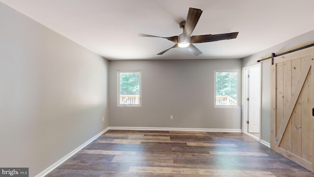 unfurnished bedroom with ceiling fan, a barn door, and dark hardwood / wood-style flooring