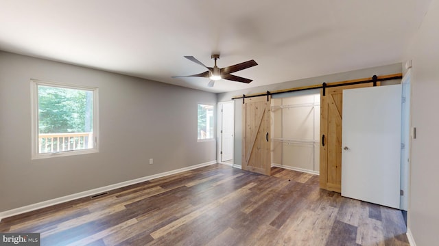 unfurnished bedroom with dark wood-type flooring, ceiling fan, a barn door, and multiple windows