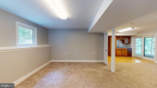 basement featuring sink, a healthy amount of sunlight, and light colored carpet