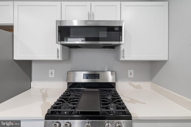 kitchen featuring light stone countertops, stainless steel appliances, and white cabinetry