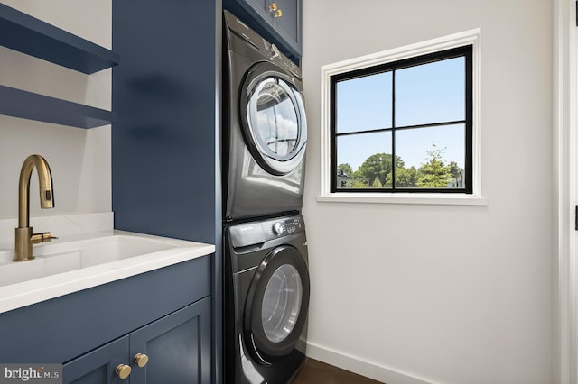 laundry area featuring cabinets, stacked washer / drying machine, and sink