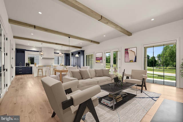 living room featuring beamed ceiling, light wood-type flooring, and a notable chandelier