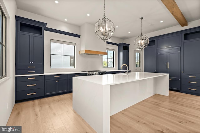 kitchen with custom exhaust hood, light hardwood / wood-style flooring, an island with sink, decorative light fixtures, and beam ceiling