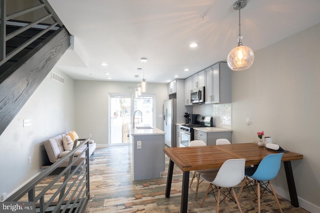 kitchen with sink, light hardwood / wood-style floors, decorative light fixtures, decorative backsplash, and appliances with stainless steel finishes