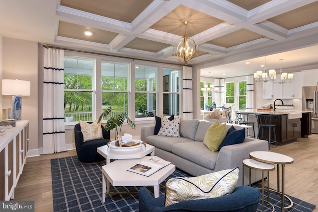 living room with coffered ceiling, an inviting chandelier, ornamental molding, and light hardwood / wood-style flooring