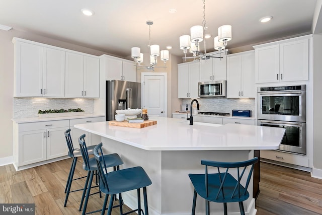 kitchen with a chandelier, white cabinets, stainless steel appliances, and light hardwood / wood-style floors