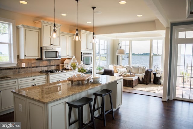 kitchen with appliances with stainless steel finishes, decorative backsplash, decorative light fixtures, a water view, and light stone counters