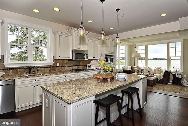 kitchen with appliances with stainless steel finishes, tasteful backsplash, a kitchen island, a water view, and sink