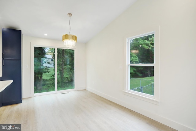 unfurnished dining area featuring an inviting chandelier, light hardwood / wood-style flooring, and a wealth of natural light