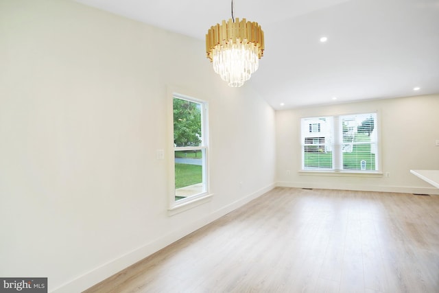 spare room featuring light hardwood / wood-style floors, a healthy amount of sunlight, vaulted ceiling, and an inviting chandelier