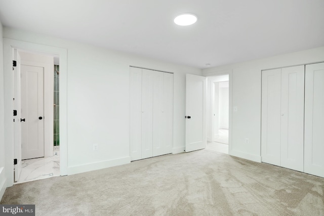 unfurnished bedroom featuring ensuite bathroom, light colored carpet, and two closets