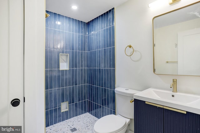 bathroom with tiled shower, vanity, and toilet